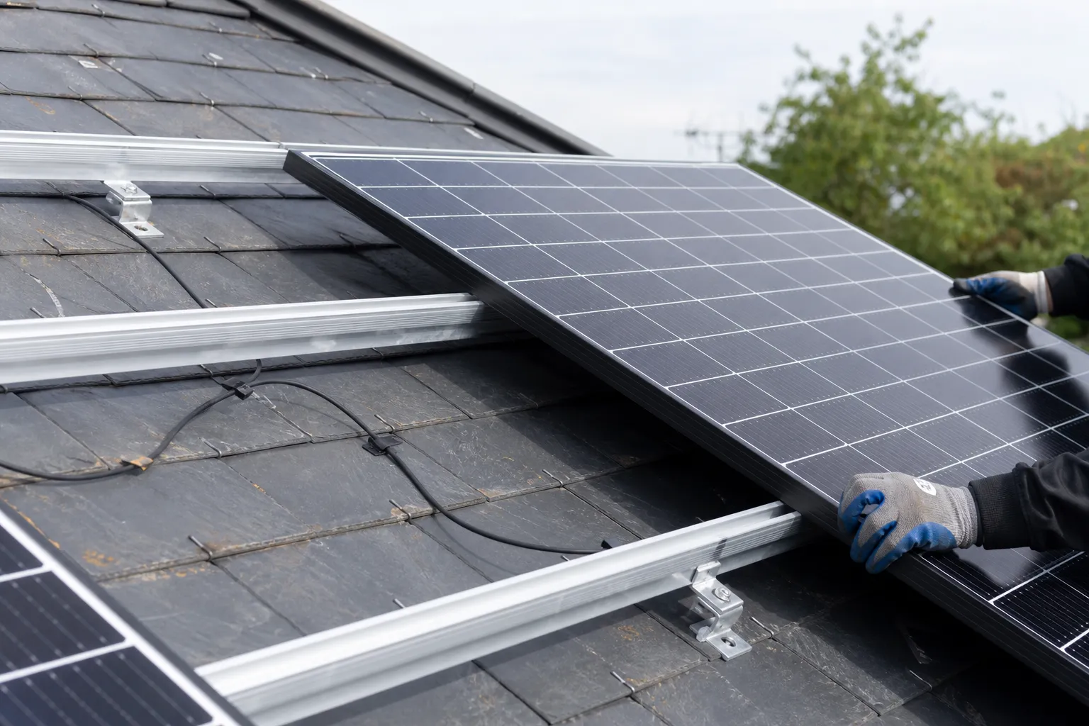 Pose de panneaux solaires en cours sur une toiture en ardoise, rails de fixation et câblage propre